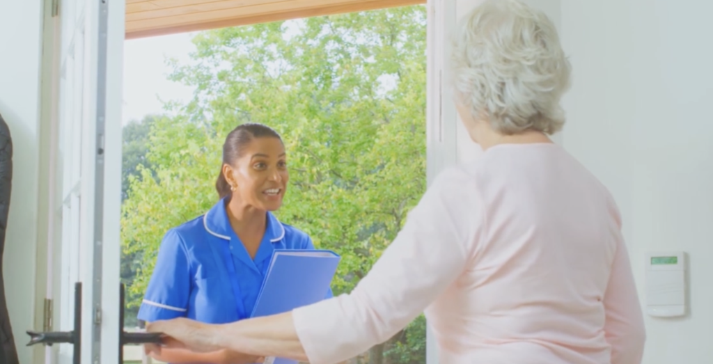 Carer providing help around the home by supporting an older adult with light household tasks.